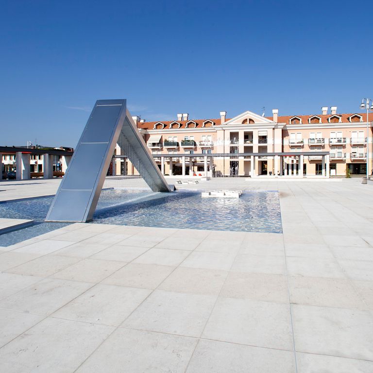 Application image for Grolla Beige Limestone. The image shows this material being used for pool coping, patio pavers and pool deck pavers. The surface finish shown is flamed. Dominant colors shown are beige, gray and white; with pink and cream secondaries. The color mix creates a cool feeling. Regular color pattern.