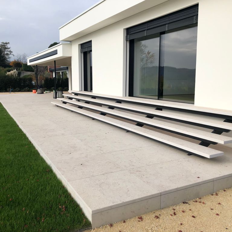 Application image for Veneto Beige Limestone. The image shows this material being used for patio pavers and treads. The surface finish shown is flamed. Dominant colors shown are beige, tan and cream; with blue, pink and tan secondaries. The color mix creates a warm feeling. Regular color pattern. Contains mineral inclusions.