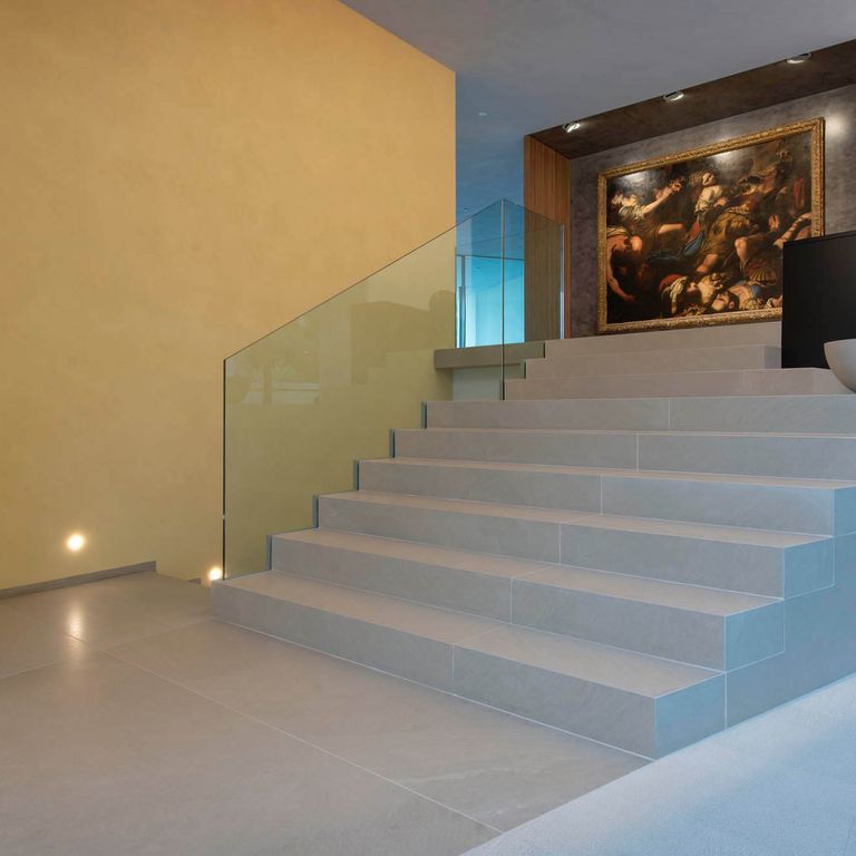 Application image for Giallo Avorio Limestone. The image shows this material being used for interior floor and monolithic steps. The surface finish shown is honed. Dominant colors shown are blue and gray; with brown, green, orange/rust and tan secondaries. The color mix creates a warm feeling. Solid color pattern.