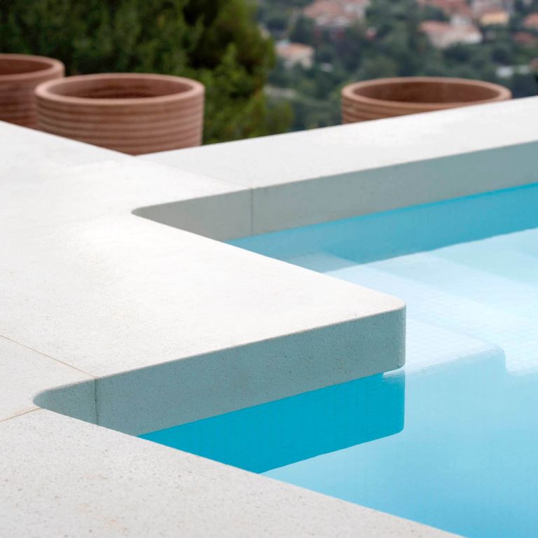 Application image for Giallo Avorio Limestone. The image shows this material being used for pool coping and pool deck pavers. The surface finish shown is honed. Dominant colors shown are gray, white and cream; with a pink secondary. The color mix creates a cool feeling. Solid color pattern.