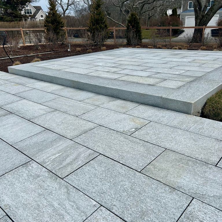 Feature image for Pietra Italia Blue/Gray Gneiss. The image shows this material being used in a patio pavers application. The surface finish shown is sand blasted. Dominant colors shown are blue and gray. The color mix creates a cool feeling.