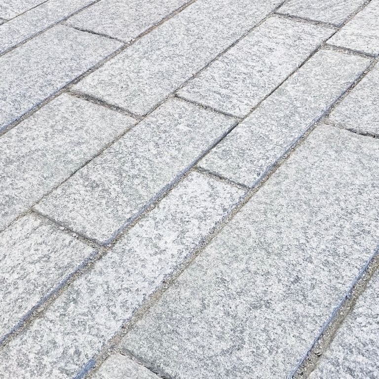 Best close-up image for Pietra Italia Gneiss - Blue. The image shows this material being used in a patio pavers application. The surface finish shown is flamed. Dominant colors shown are gray and white; with blue, pink and cream secondaries. The color mix creates a cool feeling. Fine speckled and random color patterns. Contains some mica and mineral inclusions.