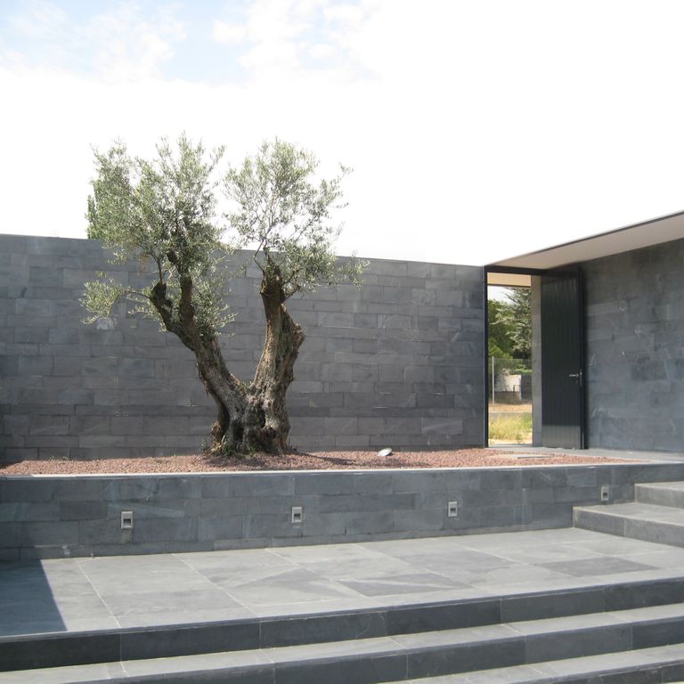 Application image for Iberian Gray Slate. The image shows this material being used for patio pavers, monolithic steps, full bed veneer and retaining wall. The surface finish shown is a combination of flamed and natural cleft. The dominant color shown is gray.