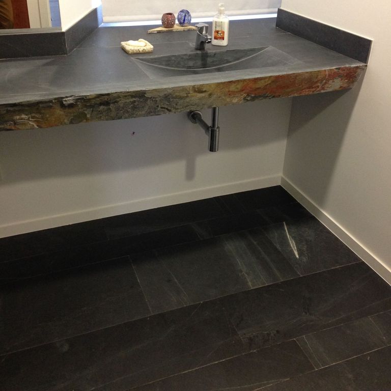 Application image for Iberian Gray Slate. The image shows this material being used for interior floor, countertop slabs and sinks. The surface finish shown is a combination of flamed, honed and natural. Dominant colors shown are black and gray. Linear and blotched color patterns.