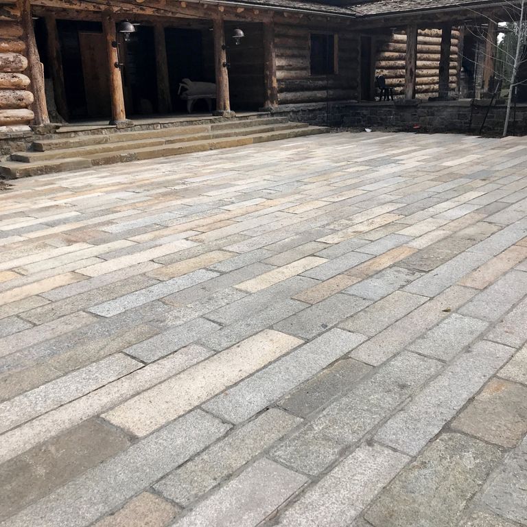 The image shows this material being used in a patio pavers application. The dominant color shown is gray; with beige, brown, white, tan and cream secondaries. Regular and fine speckled color patterns.