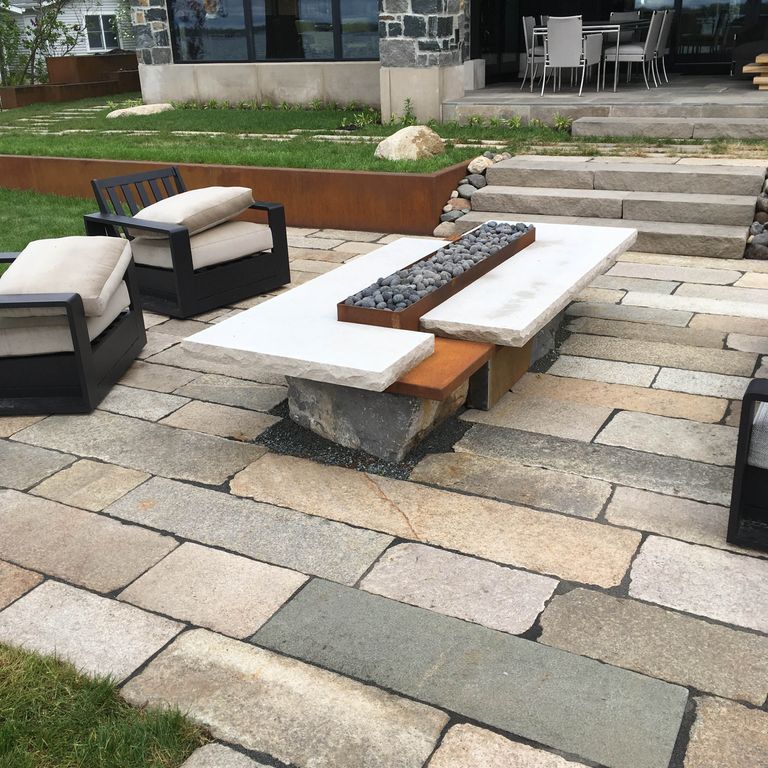 The image shows this material being used in a patio pavers application. The surface finishes shown are weathered and worn. Dominant colors shown are gray and tan; with beige, brown and orange/rust secondaries. The color mix creates a warm feeling. Regular and fine speckled color patterns.