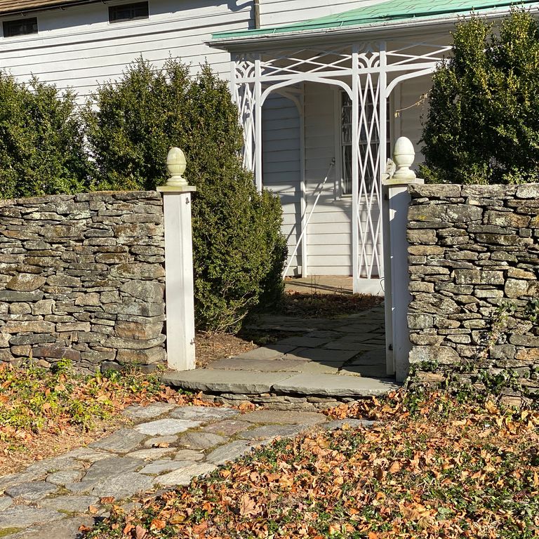 Application image for New England Fieldstone Flats. The image shows this material being used in a landscape wallstone application. The surface finish shown is weathered. Dominant colors shown are brown, gray and tan; with beige, green, orange/rust, white and cream secondaries. Exhibits 