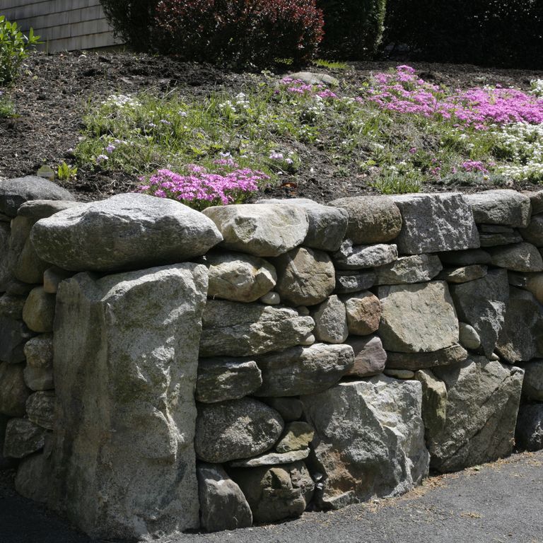 Application image for New England Fieldstone Mix. The image shows this material being used in a landscape wallstone application. The surface finish shown is weathered. The dominant color shown is gray.