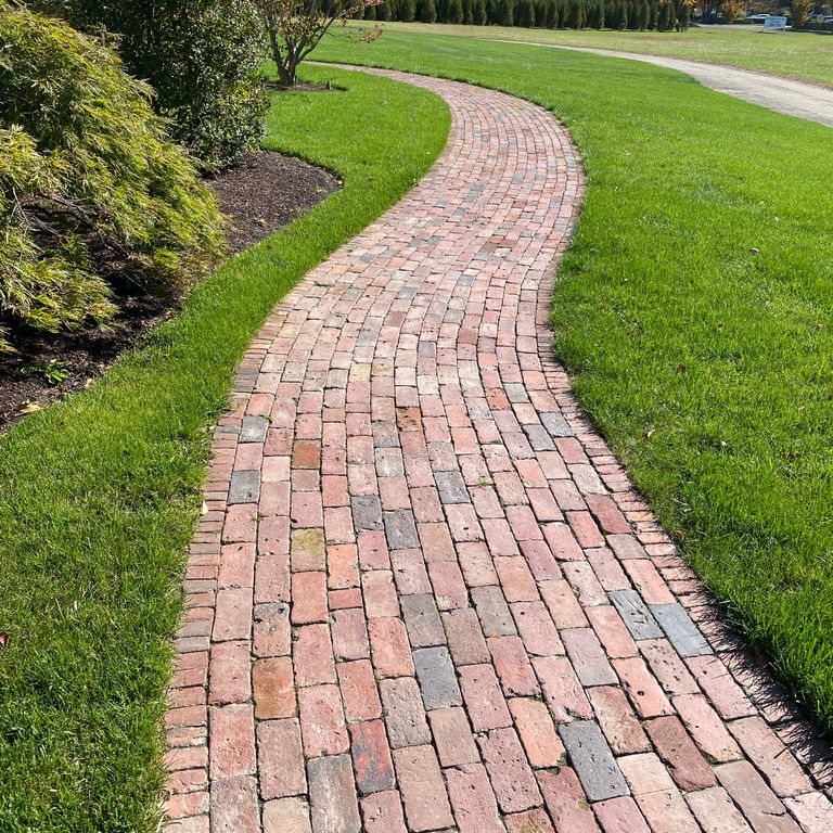Feature image for Reclaimed Brick. The image shows this material being used in a path pavers application. Dominant colors shown are pink and red; with brown, gray, orange/rust, purple and tan secondaries. The color mix creates a warm feeling. Regular color pattern.