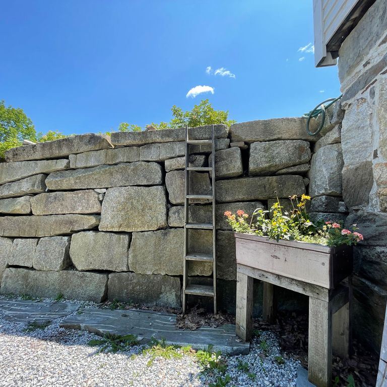 Application image for Reclaimed Granite Block. The image shows this material being used in a landscape wallstone application. The surface finish shown is split-face. The dominant color shown is gray; with a green secondary. The color mix creates a warm feeling. Speckled color pattern.