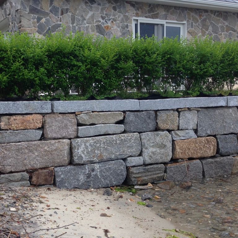Application image for Reclaimed Granite Block. The image shows this material being used in a landscape wallstone application. Dominant colors shown are black and gray. The color mix creates a warm feeling.
