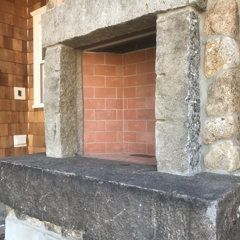 Application image for Reclaimed Granite Block. The image shows this material being used for fireplace hearth, fireplace mantel and fireplace surround. The dominant color shown is gray. The color mix creates a warm feeling.