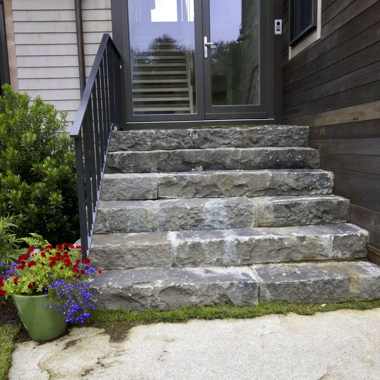 Application image for Reclaimed Granite Block. The image shows this material being used in a monolithic steps application. The surface finish shown is a combination of split-face with flat plane and weathered. The dominant color shown is gray; with black, blue, brown and white secondaries. The color mix creates a cool feeling. Blotched color pattern.