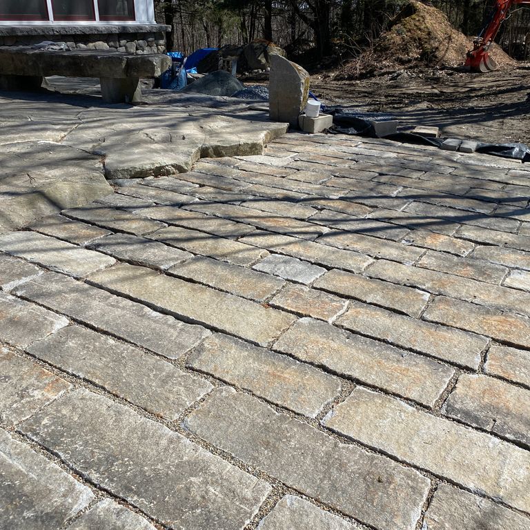 The image shows this material being used for driveway pavers and patio pavers. The dominant color shown is gray; with beige, brown, orange/rust and tan secondaries. The color mix creates a warm feeling.