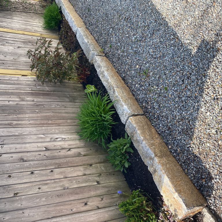 Application image for Reclaimed Granite Curbstone - Junior. The image shows this material being used in a landscape curbing & edging application. This is a building and landscape stone for indoor and outdoor commercial and residential applications. Suitable for general use, freeze-thaw conditions, low heat absorption surfaces, high traffic areas and low slipperiness surfaces situations. Moderate to higher on the price spectrum.