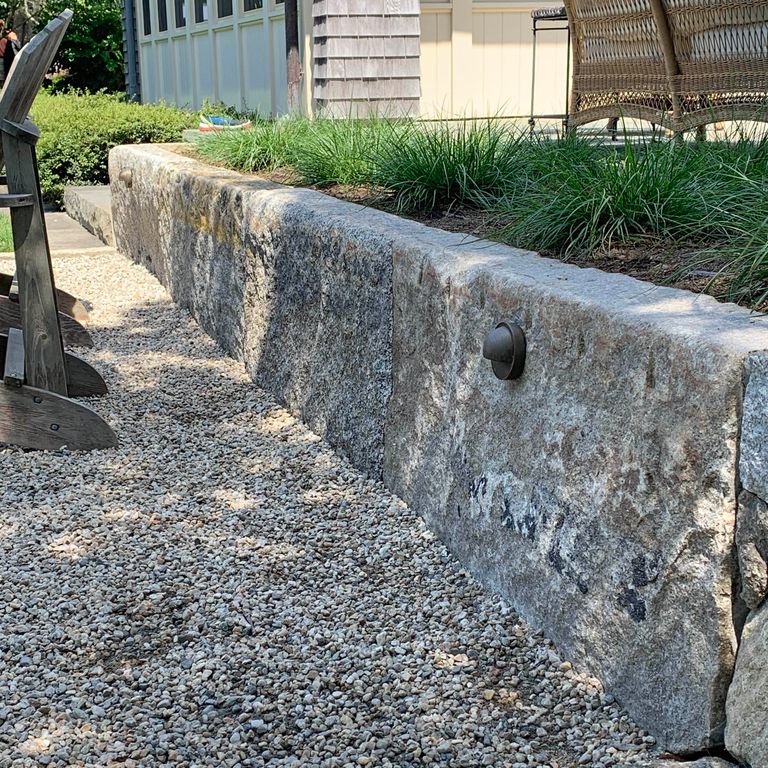 Application image for Reclaimed Granite Curbstone - Jumbo. The image shows this material being used for landscape wallstone and landscape curbing & edging. The surface finish shown is a combination of weathered and worn. The dominant color shown is gray; with a brown secondary. The color mix creates a cool feeling. Speckled, blotched and random color patterns.