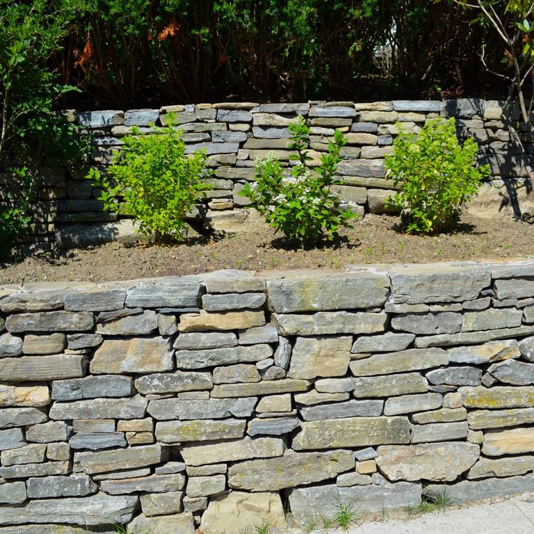 Application image for Mystic Mountain - Natural. The image shows this material being used in a landscape wallstone application. The surface finish shown is split-face. The dominant color shown is gray. The color mix creates a warm feeling. Regular color pattern.