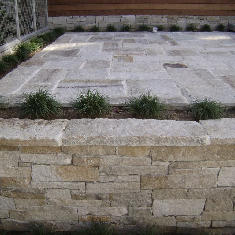 The image shows this material being used in a wallstone cap application. The dominant color shown is gray; with brown, orange/rust, white and tan secondaries. Regular and fine speckled color patterns.