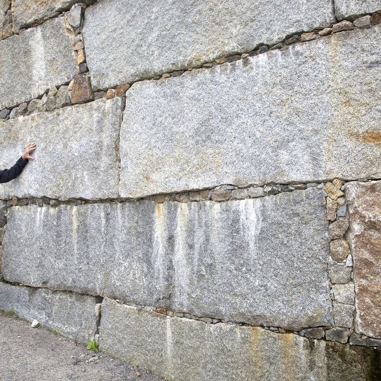 Feature image for Reclaimed Granite Bridge Blocks. The image shows this material being used in a landscape wallstone application. The design pattern shown is dimensional squares & rectangles. The dominant color shown is gray; with beige, brown, orange/rust, white and cream secondaries. The color mix creates a warm feeling.
