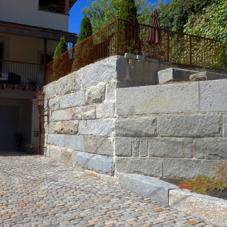 Application image for Granite - Reclaimed Bridge Blocks. The image shows this material being used for landscape wallstone and driveway pavers. The dominant color shown is gray.