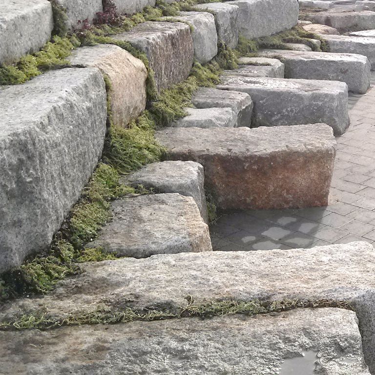 Application image for Reclaimed Granite Bridge Blocks. The image shows this material being used for seating & benches and landscape wallstone. The surface finish shown is weathered. The dominant color shown is gray; with beige, brown, white and tan secondaries. Regular and blotched color patterns.