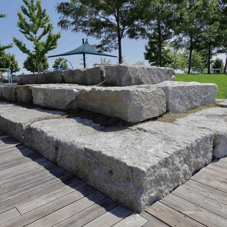 Application image for Reclaimed Granite Bridge Blocks. The image shows this material being used in a seating & benches application. The surface finish shown is a combination of chiseled and weathered. The dominant color shown is gray. The color mix creates a cool feeling.