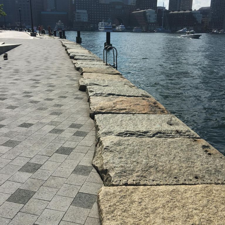 Application image for Reclaimed Granite Bridge Blocks. The image shows this material being used for landscape wallstone and full bed veneer. The surface finish shown is weathered. Dominant colors shown are brown, gray and tan; with beige and orange/rust secondaries. The color mix creates a cool feeling. Regular and blotched color patterns.
