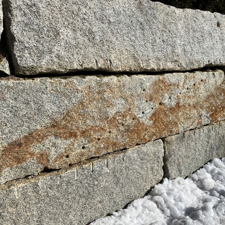 Application image for Reclaimed Granite Bridge Blocks. The image shows this material being used in a landscape wallstone application. The surface finish shown is weathered. The dominant color shown is gray; with brown, orange/rust and tan secondaries.