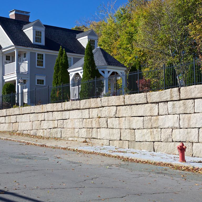 Application image for Reclaimed Granite Bridge Blocks. The image shows this material being used in a landscape wallstone application. The surface finish shown is weathered. Dominant colors shown are beige and gray; with orange/rust, tan and cream secondaries. The color mix creates a warm feeling.