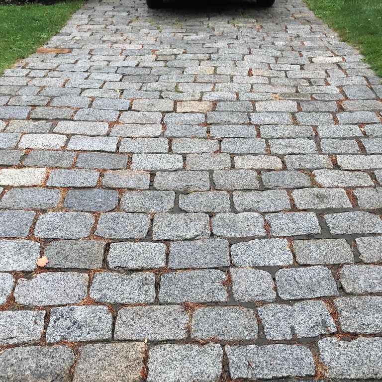 The image shows this material being used in a driveway pavers application. The dominant color shown is gray; with beige, black and brown secondaries.