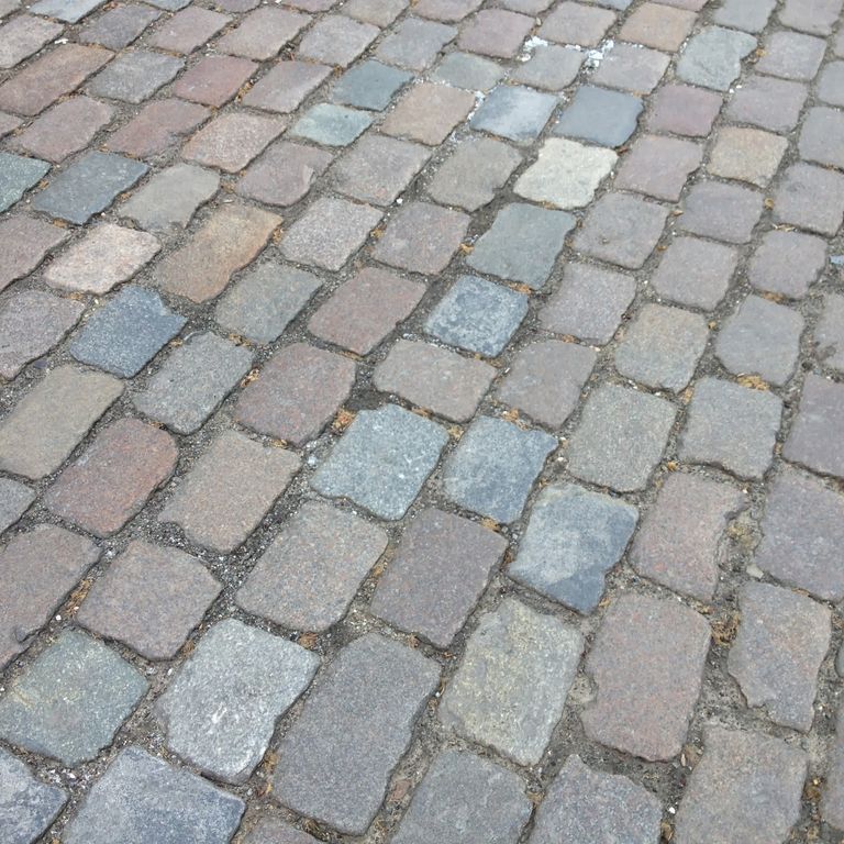 Application image for Granite - Reclaimed Swedish Cobblestones. The image shows this material being used in a driveway pavers application. The surface finish shown is antiqued. The dominant color shown is gray.
