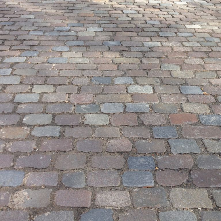 Application image for Granite - Reclaimed Swedish Cobblestones. The image shows this material being used for driveway pavers and path pavers. The surface finish shown is antiqued. The dominant color shown is gray. The color mix creates a warm feeling.