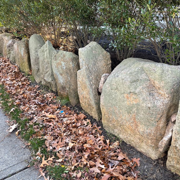 Application image for New England Fieldstone Boulders & Ledgestone. The image shows this material being used in a landscape wallstone application. The surface finish shown is weathered. The dominant color shown is gray. The color mix creates a warm feeling.