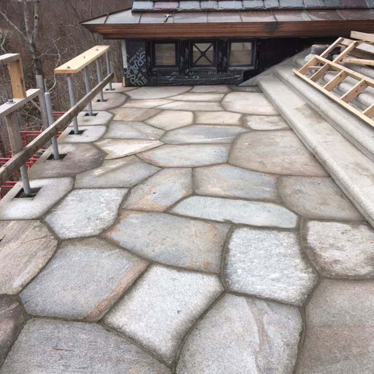 Application image for New England Fieldstone Boulders & Ledgestone. The image shows this material being used in a patio pavers application. The surface finish shown is weathered. The dominant color shown is gray; with beige, blue, brown, white, tan and cream secondaries. Regular color pattern.