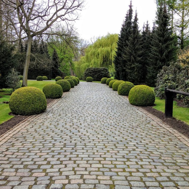 Feature image for Reclaimed European Porphyry Cobblestones. The image shows this material being used in a driveway pavers application. The surface finish shown is . The dominant color shown is gray; with beige, brown, orange/rust, purple, white and tan secondaries. The color mix creates a warm feeling. Regular, fine speckled and speckled color patterns.