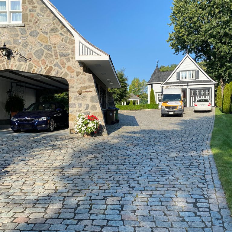 Application image for Reclaimed European Porphyry Cobblestones. The image shows this material being used in a driveway pavers application. The surface finish shown is . Dominant colors shown are beige and tan. The color mix creates a warm feeling. Fine speckled color pattern.