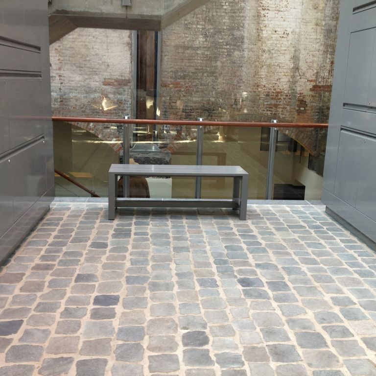 Application image for Porphyry - Reclaimed European Cobblestones. The image shows this material being used in an interior floor application. The surface finish shown is sawn. The dominant color shown is gray. The color mix creates a warm feeling.