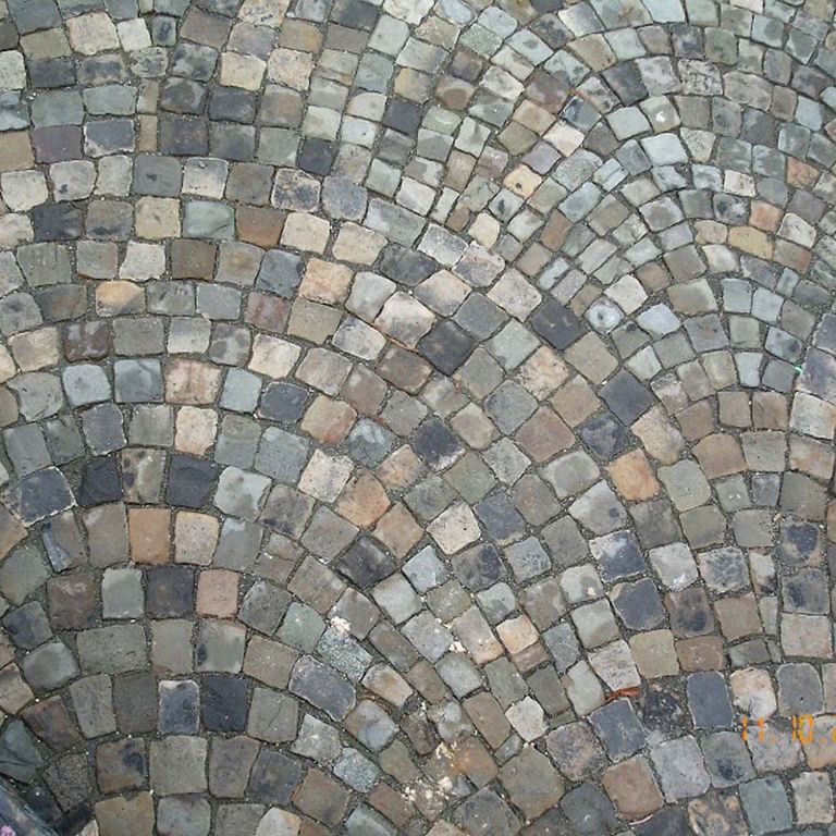 Application image for Reclaimed European Sandstone Cobblestones. The image shows this material being used in a driveway pavers application. The surface finish shown is . The dominant color shown is gray; with beige, black, blue, brown, orange/rust, purple, white and tan secondaries. The color mix creates a cool feeling. Regular color pattern.