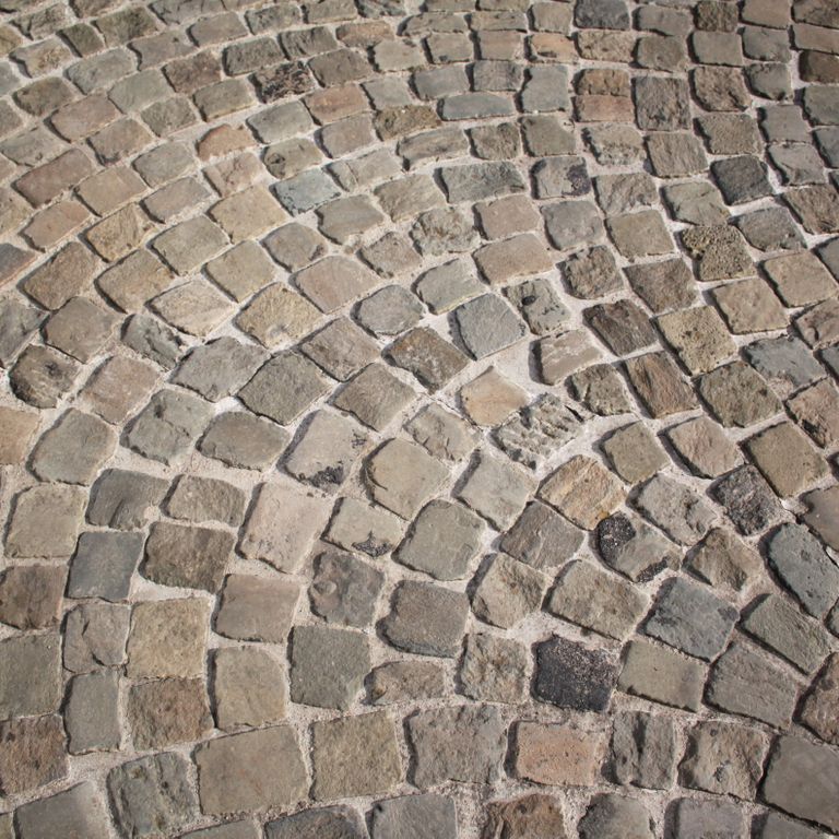 Application image for Reclaimed European Sandstone Cobblestones. The image shows this material being used in a driveway pavers application. The surface finish shown is . Dominant colors shown are brown, gray and tan. The color mix creates a warm feeling.