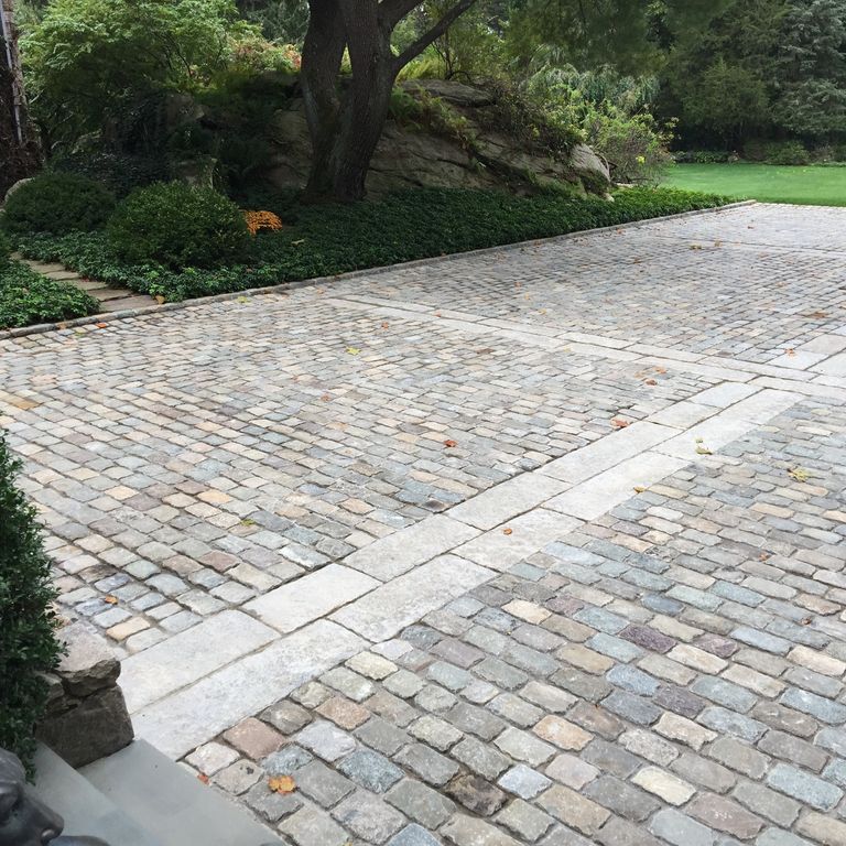 Application image for Reclaimed European Sandstone Cobblestones. The image shows this material being used in a driveway pavers application. The surface finish shown is . The dominant color shown is gray. The color mix creates a warm feeling.