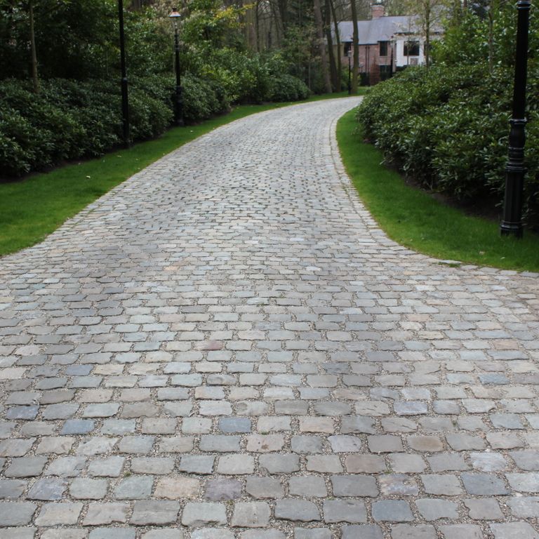 Application image for Reclaimed European Sandstone Cobblestones. The image shows this material being used in a driveway pavers application. The surface finish shown is . The dominant color shown is gray; with beige, blue, brown and white secondaries. The color mix creates a warm feeling.