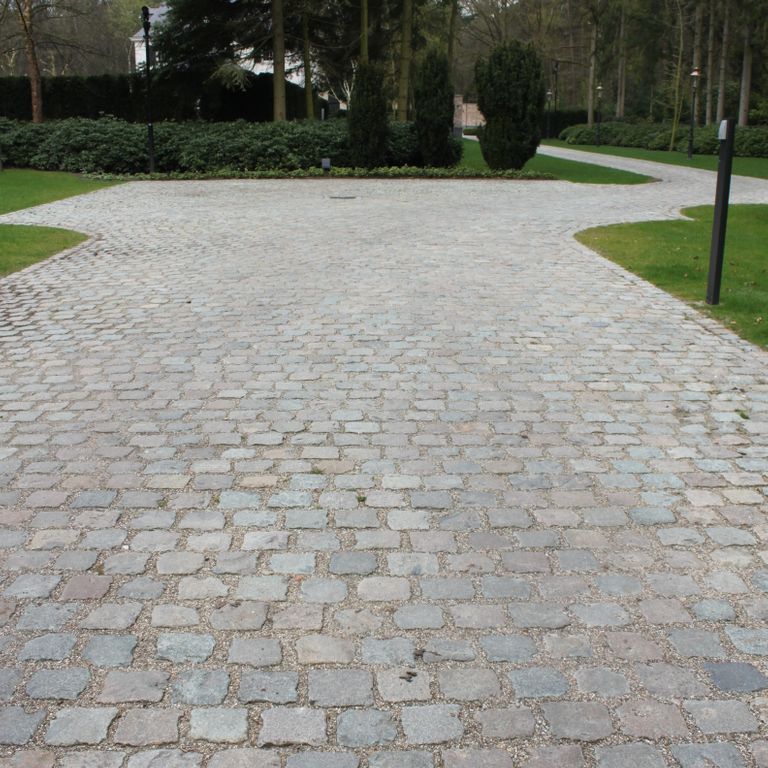Application image for Reclaimed European Sandstone Cobblestones. The image shows this material being used in a driveway pavers application. The surface finish shown is . The dominant color shown is gray. The color mix creates a cool feeling.