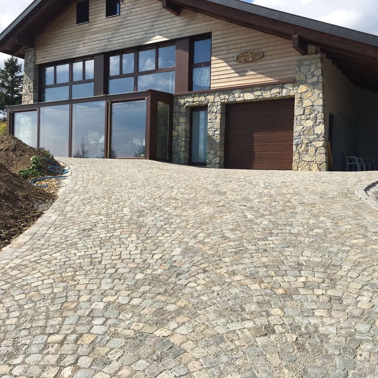 Application image for Reclaimed European Sandstone Cobblestones. The image shows this material being used in a driveway pavers application. The surface finish shown is . Dominant colors shown are beige, gray and tan. The color mix creates a warm feeling.
