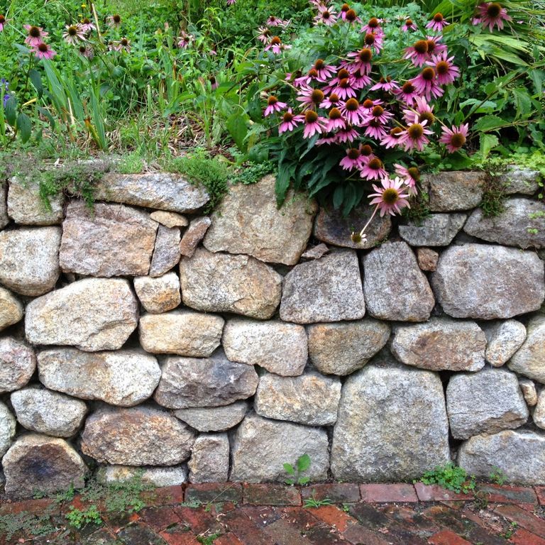 Application image for New England Fieldstone Rounds. The image shows this material being used in a landscape wallstone application. The surface finish shown is weathered. The dominant color shown is gray.