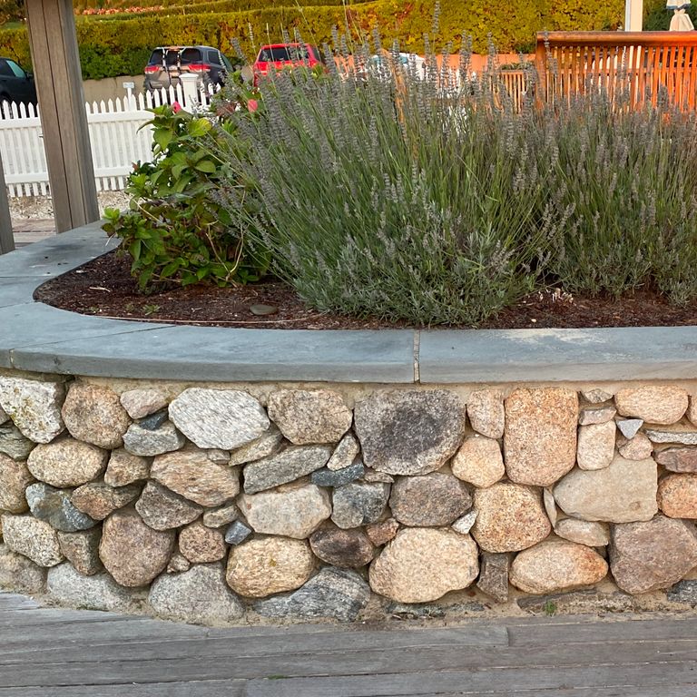 Application image for New England Fieldstone Rounds. The image shows this material being used in a landscape wallstone application. The surface finish shown is weathered. The dominant color shown is gray. The color mix creates a cool feeling.