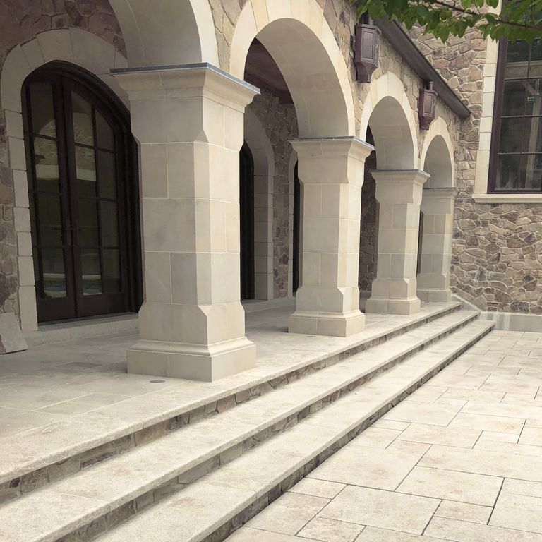 Application image for Limestone - Mountain Hard Beige. The image shows this material being used for architectural elements, patio pavers, columns and treads. Dominant colors shown are beige, tan and cream; with gray and white secondaries. The color mix creates a warm feeling. Regular and cloudy color patterns.