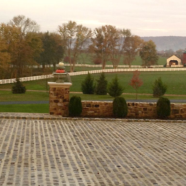 Feature image for Reclaimed Midwest Sandstone Cobblestones. The image shows this material being used for driveway pavers and patio pavers. The dominant color shown is brown; with beige, gray, orange/rust, white, tan and cream secondaries. The color mix creates a warm feeling. Regular color pattern.