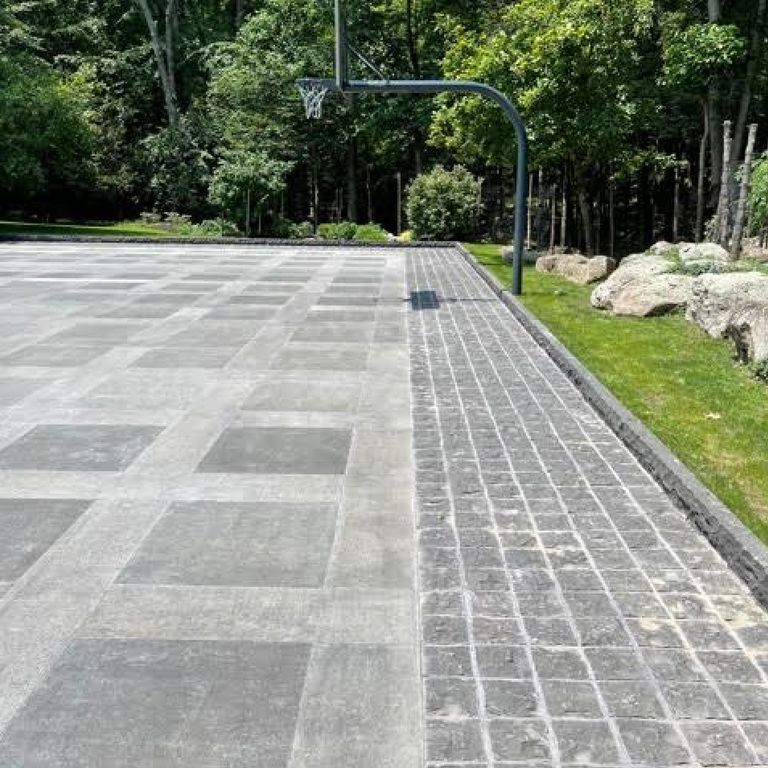 Application image for Nordic Black Basalt. The image shows this material being used in a driveway pavers application. The surface finish shown is a combination of adze, flamed and split-face. The dominant color shown is gray. Solid color pattern.