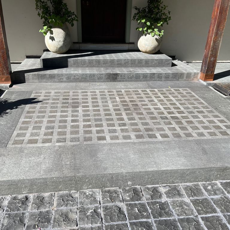 Application image for Nordic Black Basalt. The image shows this material being used for landings and monolithic steps. The surface finish shown is a combination of adze, honed and split-face. The dominant color shown is gray; with a white secondary. Solid color pattern.