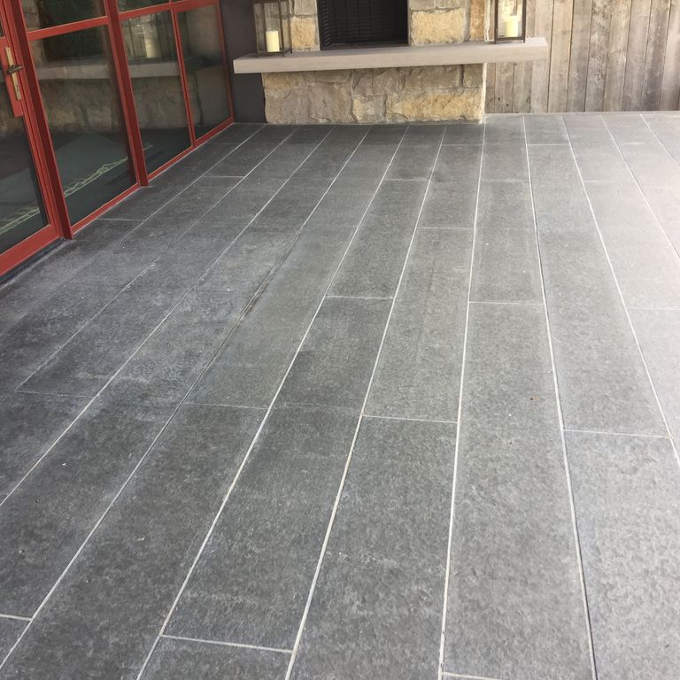 Application image for Nordic Black Basalt. The image shows this material being used in a patio pavers application. The surface finish shown is flamed. The dominant color shown is gray. The color mix creates a warm feeling. Regular color pattern.